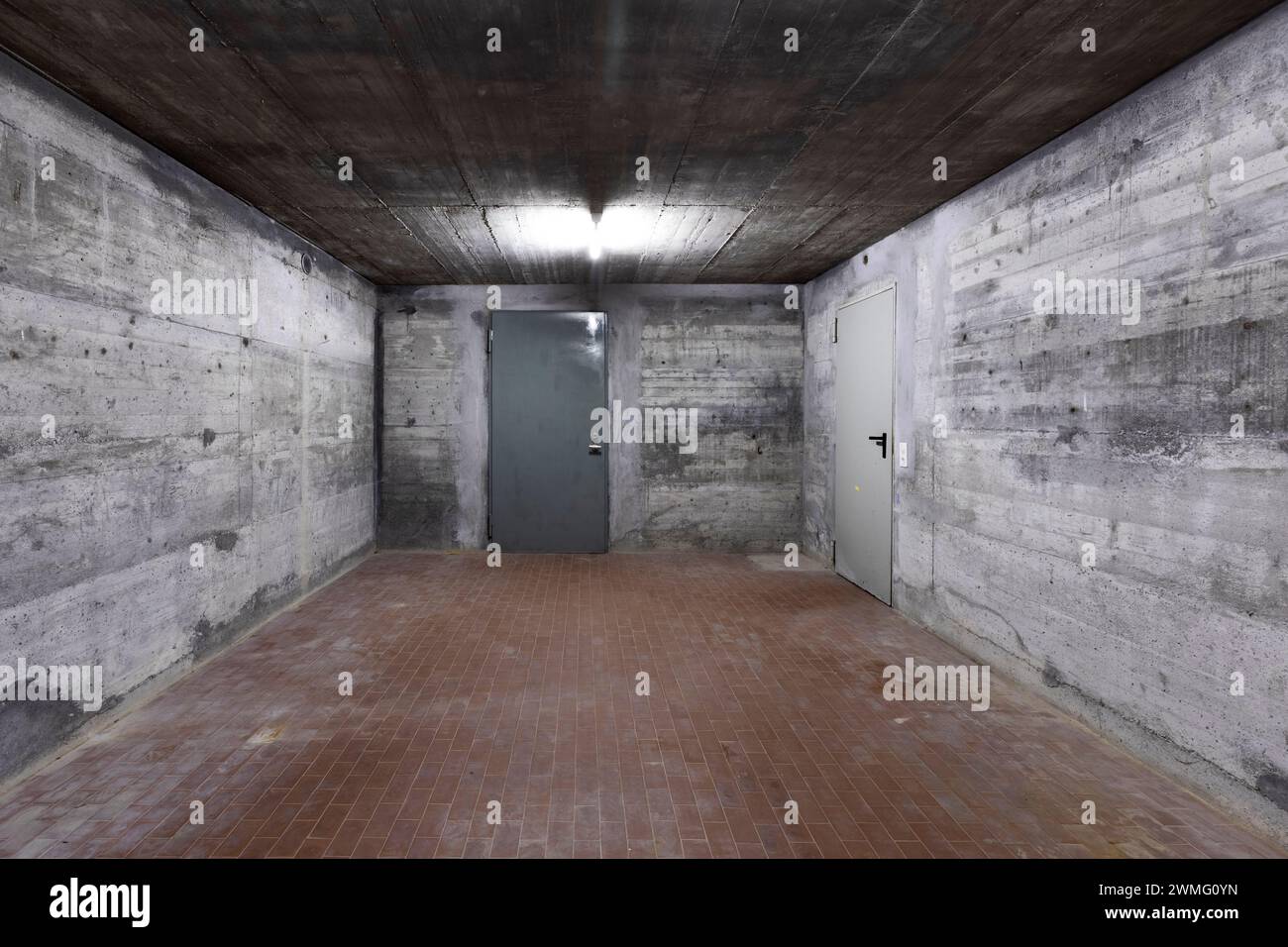 Vorderansicht der Stahlbetonwand eines Bunkers mit geschlossener gepanzerter Tür. Szene beleuchtet von einer weißen Neonlampe. Niemand drinnen Stockfoto