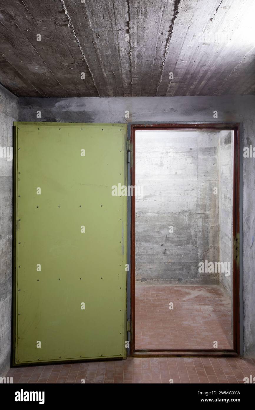 Vorderansicht der Stahlbetonwand eines Bunkers mit offener gewölbter Panzertür. Szene beleuchtet von einer weißen Neonlampe. Niemand drinnen Stockfoto