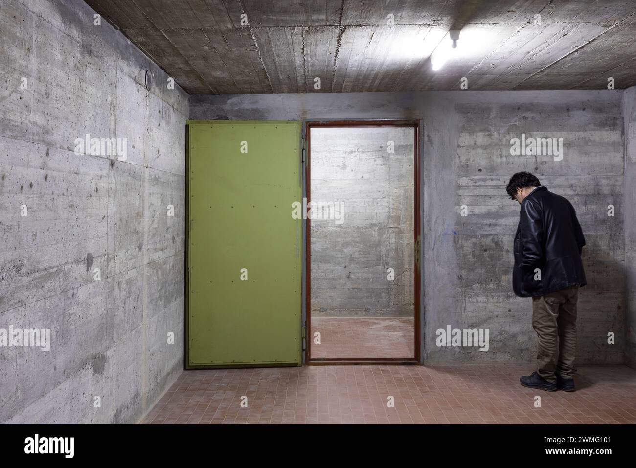 Der Mann nach unten blickt deprimiert in einem Bunker mit geöffneter Panzertür. Szene beleuchtet von einer weißen Neonlampe. Niemand drinnen Stockfoto