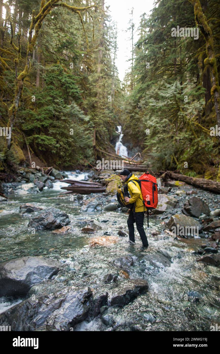 Backpacker überquert den Fluss unter einem Wasserfall Stockfoto