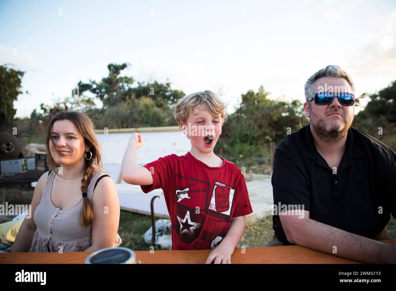 Der blonde Junge macht ein albernes Gesicht am Picknicktisch mit der Familie in der Karibik Stockfoto