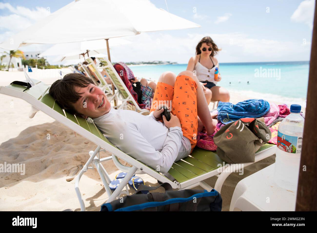 Der lächelnde Tween-Junge mit Zahnspange sitzt auf dem Beach Lounge Chair Stockfoto