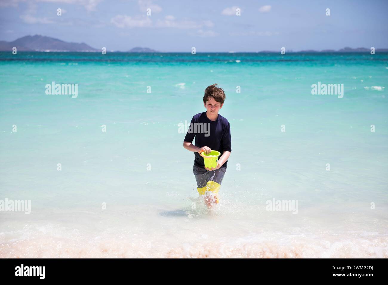 Tween Boy trägt Bucket, der am windigen Tag aus der Karibik läuft Stockfoto