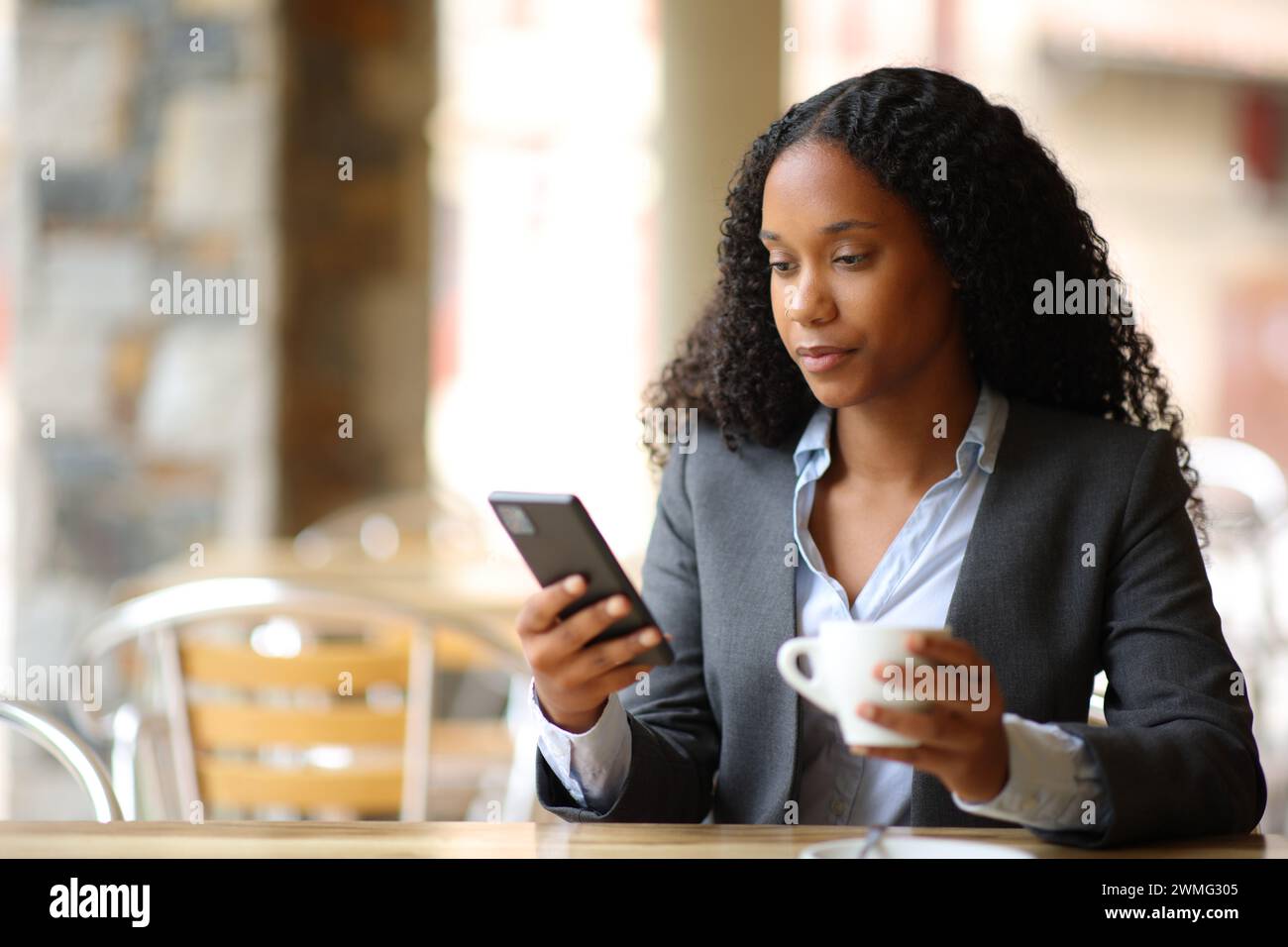 Seriöser schwarzer Manager, der das Smartphone überprüft und Kaffee auf der Bar-Terrasse trinkt Stockfoto