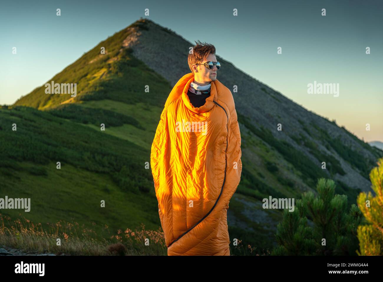 Wanderer, die im Schlafsack stehen, beobachten den Sonnenaufgang in den Bergen Stockfoto
