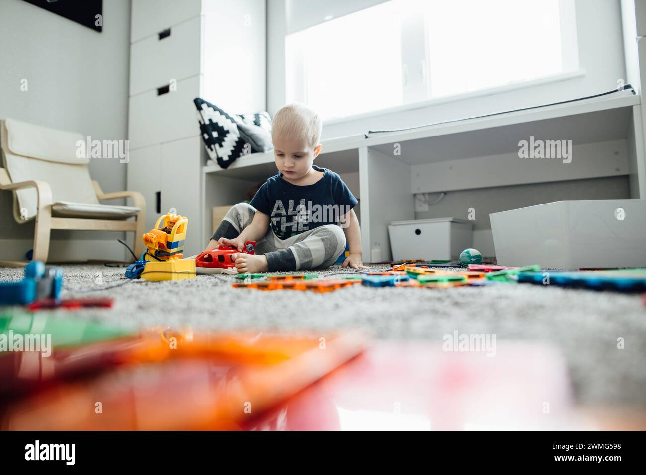 Niedriger Blick auf Kleinkinder, die mit bunten Spielzeugen in einem unordentlichen Spielzimmer spielen Stockfoto