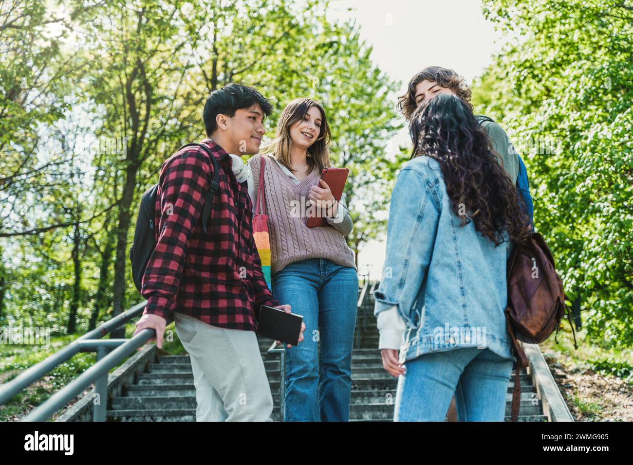 Teenager chatten im Park - zwangloses Meetup - Technologienutzung, Freunde, Outdoor-Umgebung, Campus-Leben. Stockfoto
