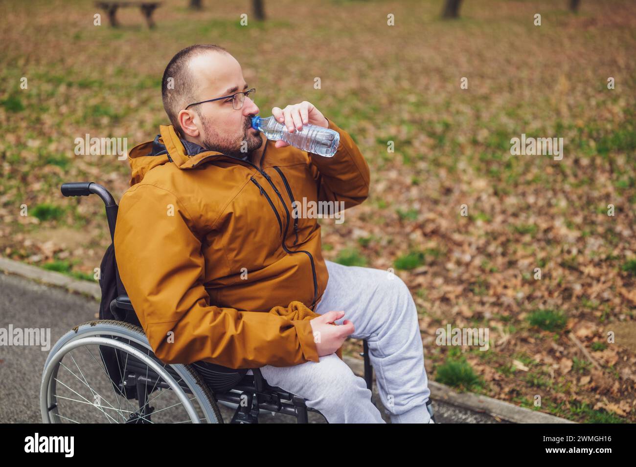 Querschnittsgelähmter behinderter Mann im Rollstuhl genießt draußen und trinkt Wasser. Stockfoto