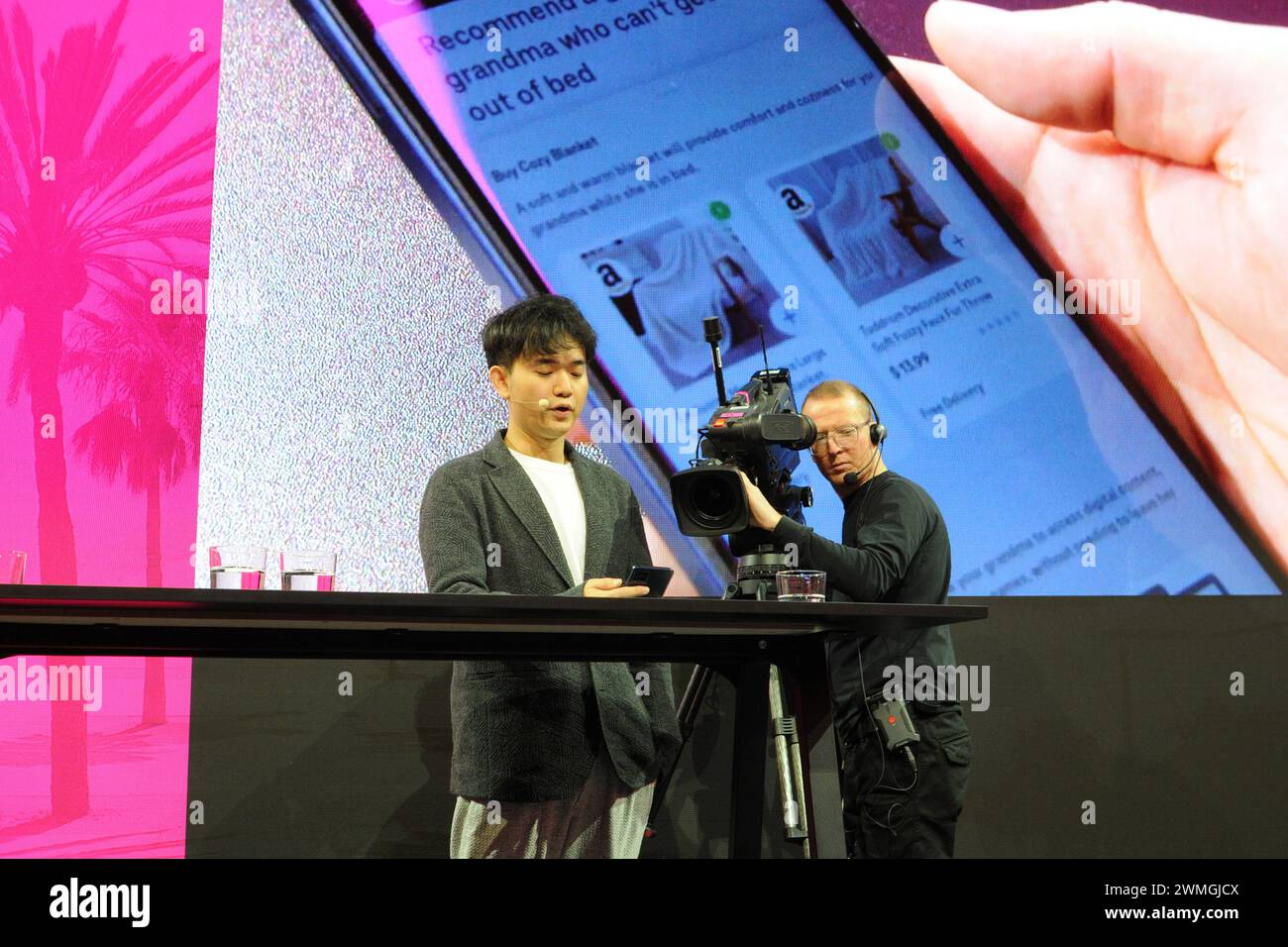 Barcelona, Spanien. Februar 2024. Jerry Yue, Gründer und CEO des US-amerikanischen Technologieunternehmens Brain Technologies, steht auf der Bühne des Mobile World Congress (MWC) und stellt einen Prototyp eines Smartphones der Deutschen Telekom vor. Auf dem Bildschirm hinter ihm sehen Sie die Geschenkvorschläge, die Yue's KI gemacht hat, auf dem Display des Telefons. Er nutzt keine Apps mehr, die KI wird über Sprachbefehle gesteuert. Quelle: Wolf von Dewitz/dpa/Alamy Live News Stockfoto