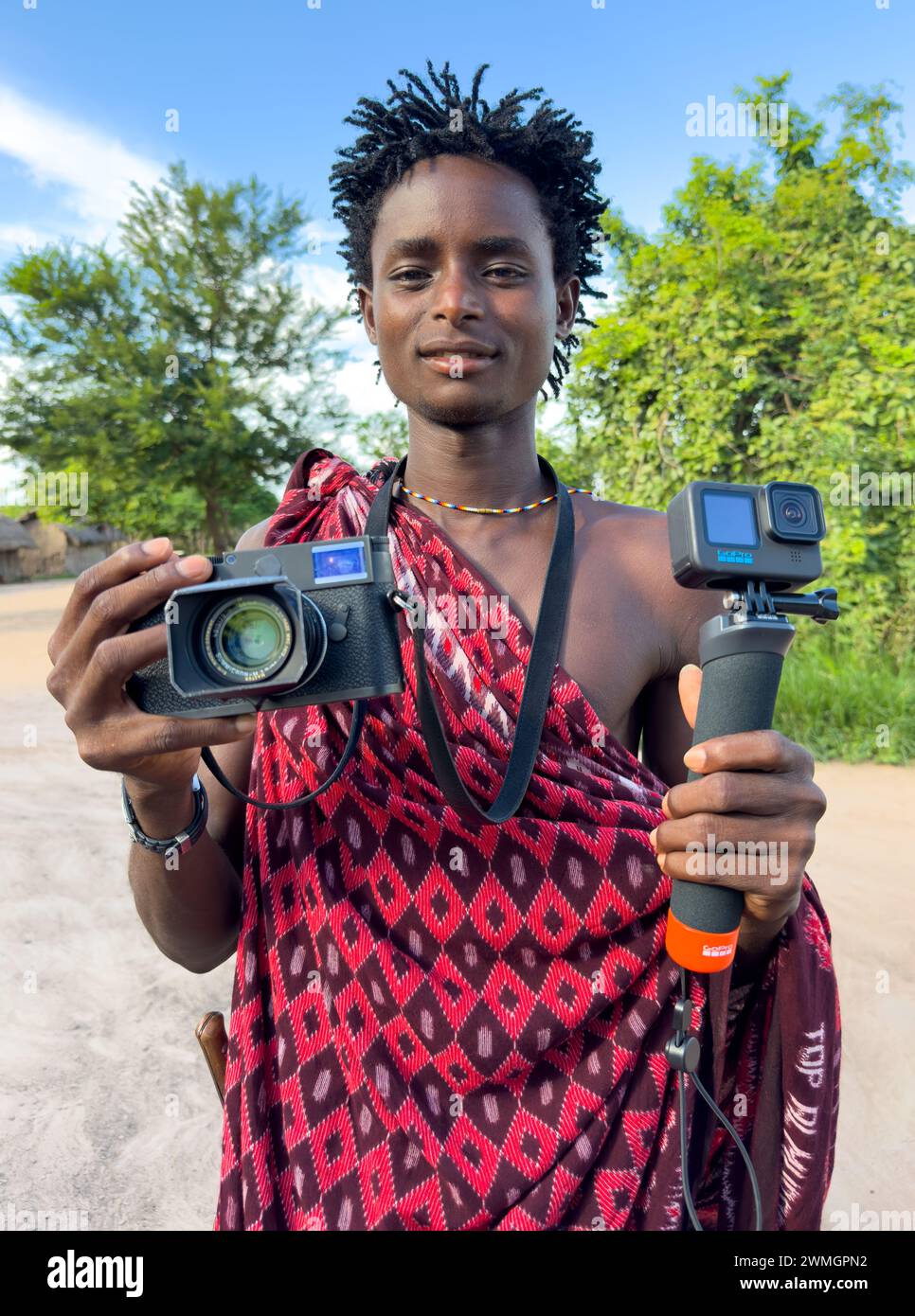 Ein junger Maasai-Krieger hält in seinem Dorf in Mikumi, Tansania, eine GoPro 11 Videokamera und eine Leica M10-R Digitalkamera. Stockfoto