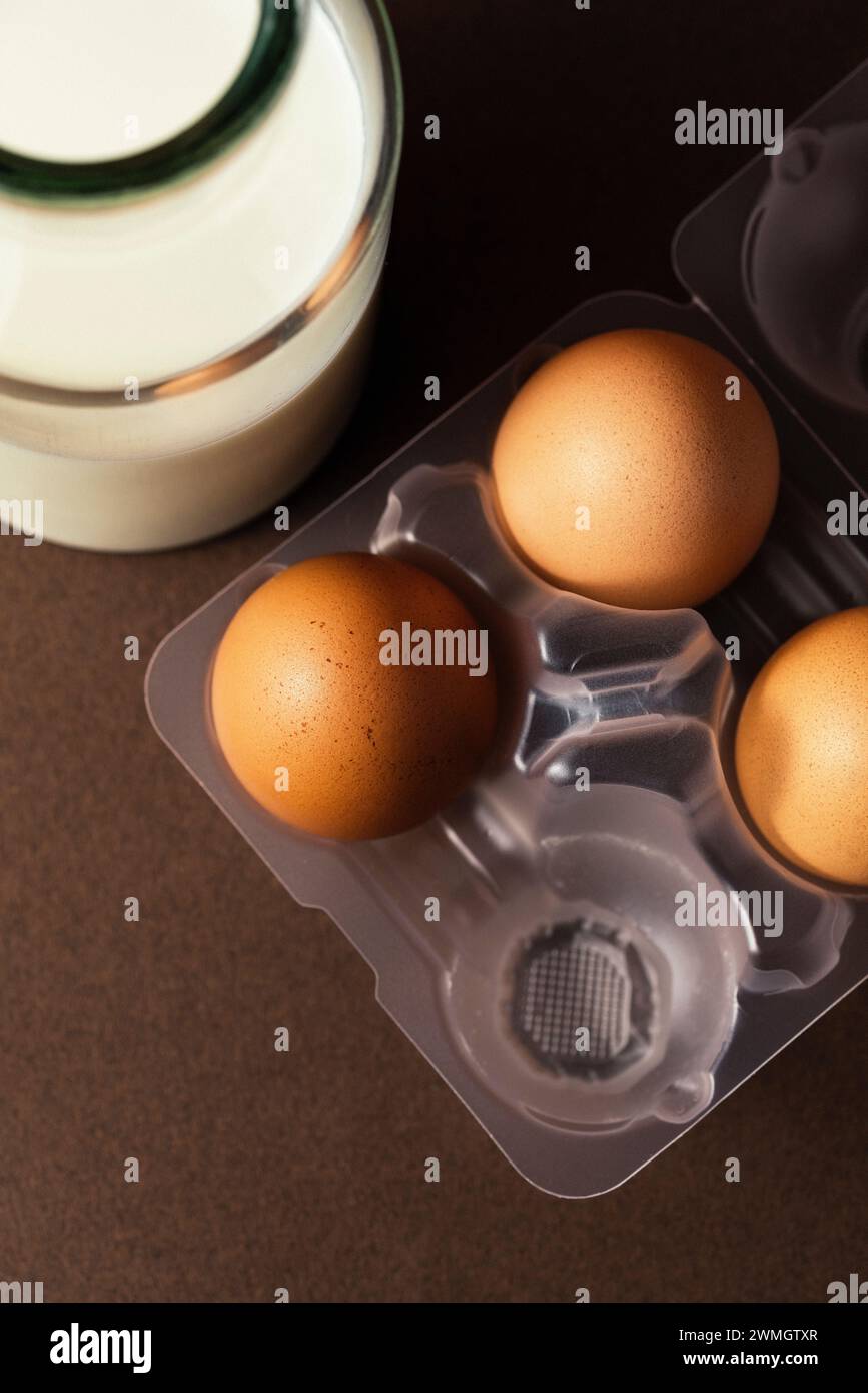 Eier in platischem Eierkasten mit einer Flasche Milch auf braunem Hintergrund. Direkt darüber, natürlicher Lichteffekt Stockfoto