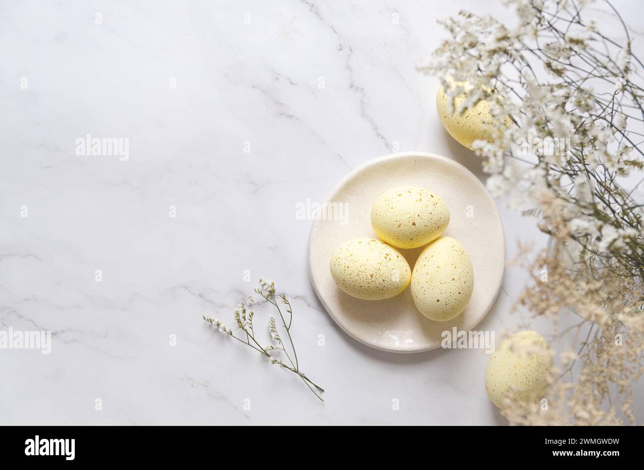 Gelbe Ostereier mit goldenen Flecken auf einem Teller und Blumen auf weißem Marmorhintergrund mit Kopierraum. Stockfoto