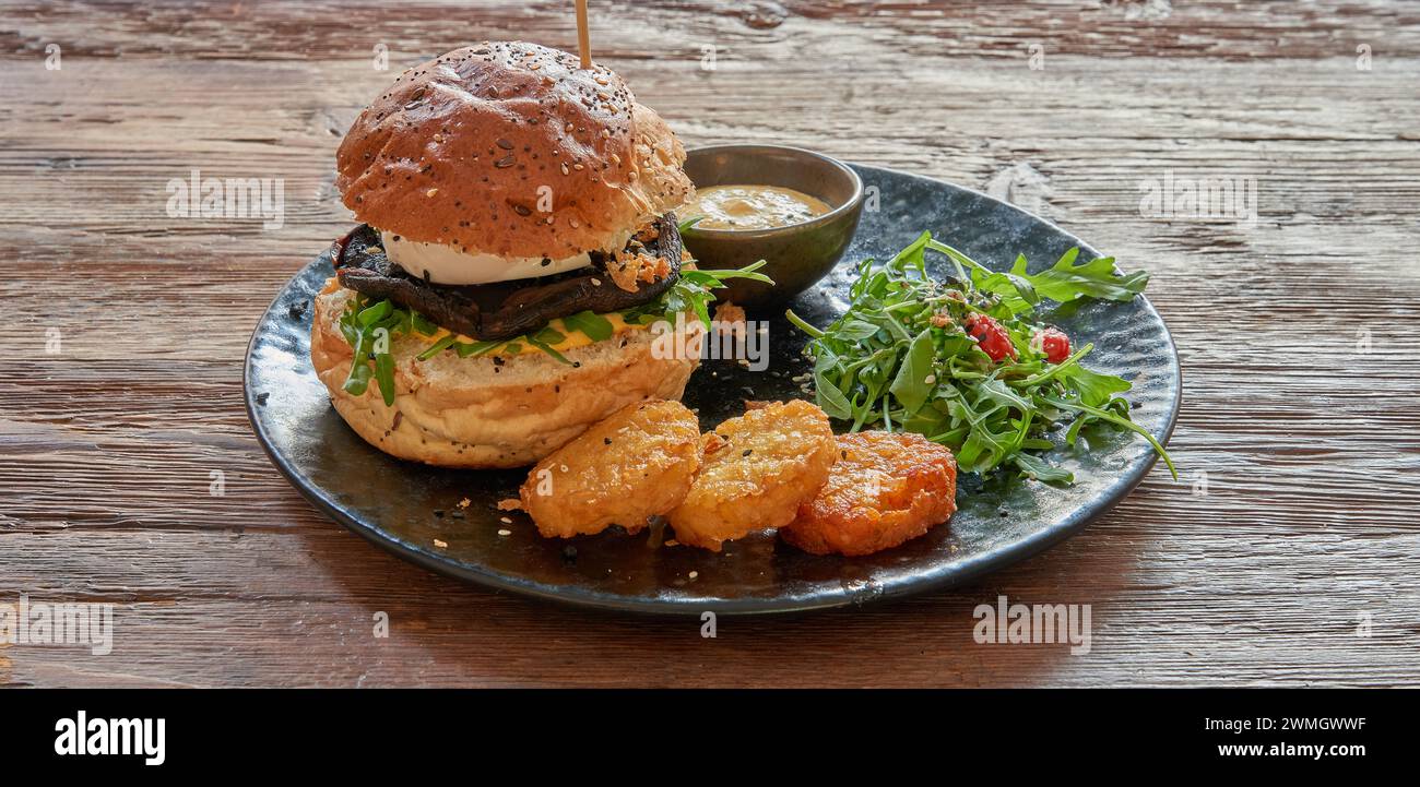Teller mit vegetarischem Burger und Rosti auf strukturiertem Holztisch Stockfoto