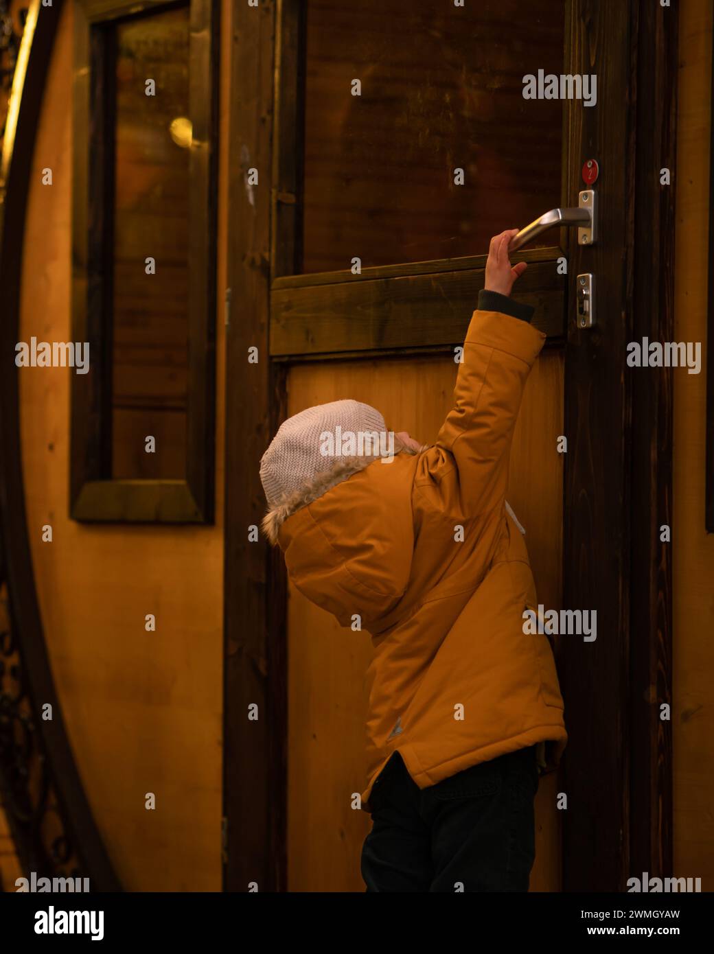 „Der Schlüssel zur Entdeckung“: Ein Kind in einer gelben Jacke und einer weißen Kappe öffnet eine Tür. Das warme Licht betont Neugier und Staunen. Eine Geschichte der Erkundung Stockfoto