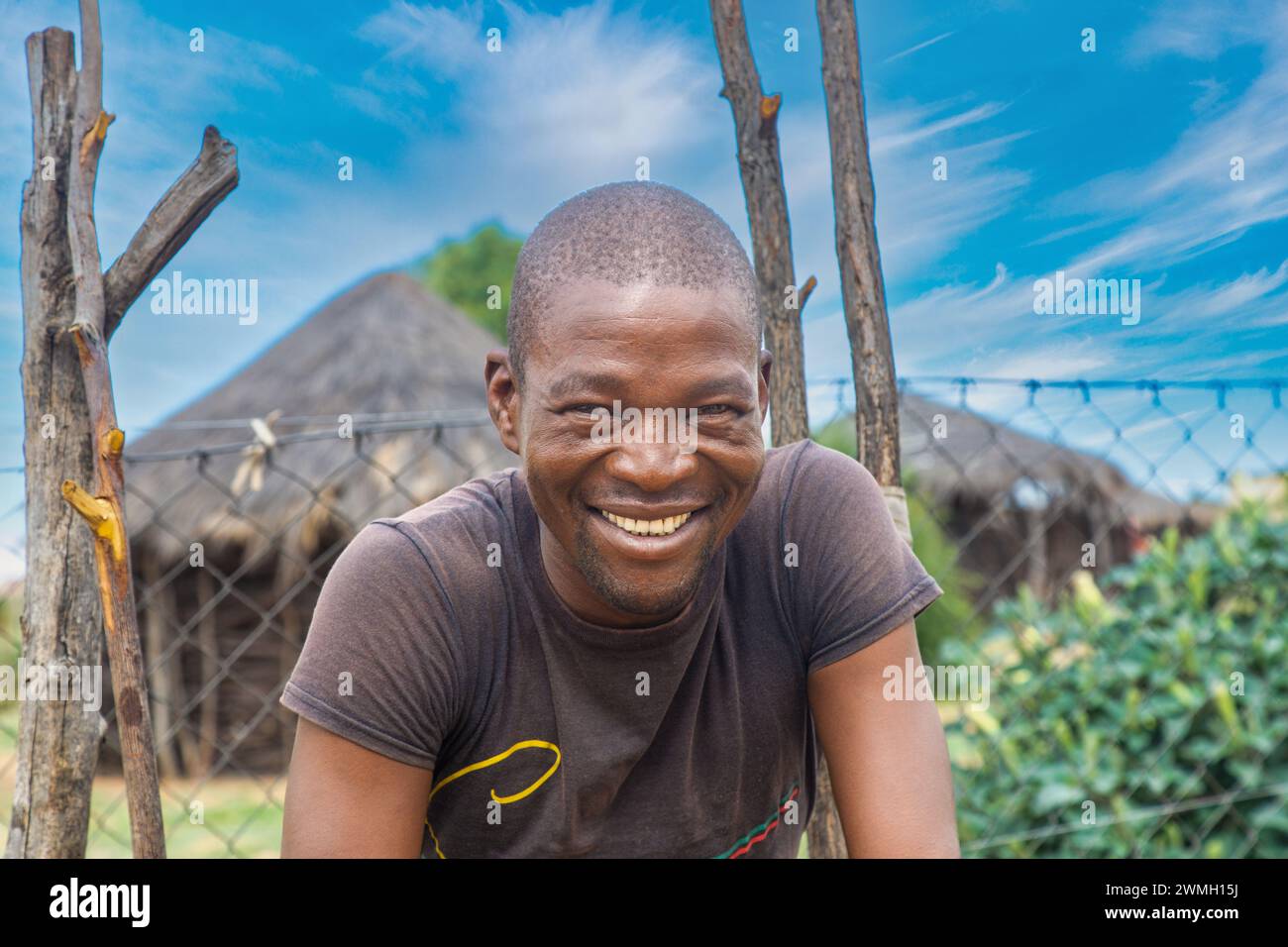 Glückliche afrikanische Männer, mit einem zahnigen Lächeln, stehen vor einer strohgedeckten Hütte. Stockfoto