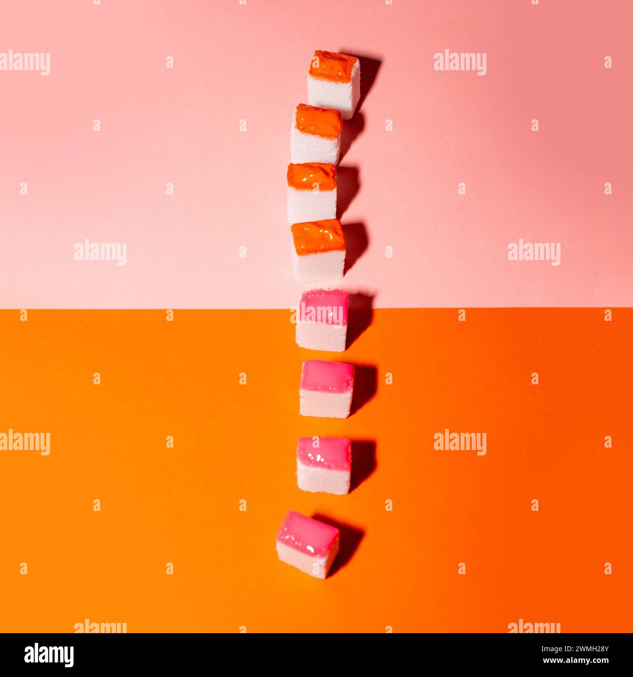 Bunte Zuckerwürfel auf orangefarbenem und rosa Hintergrund. Minimales kreatives Konzept. Stockfoto