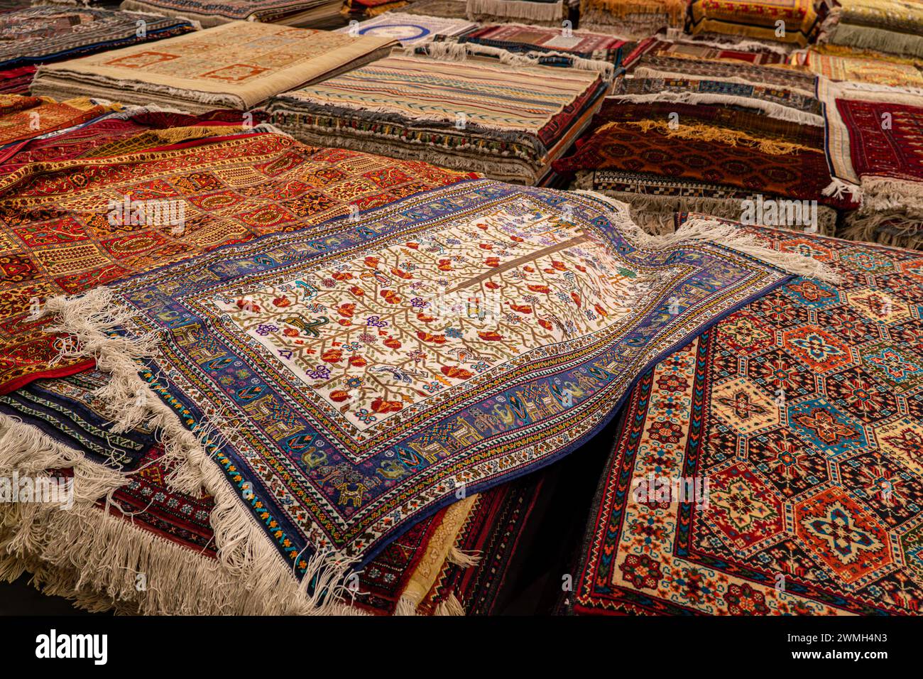 Vielfalt der herrlichen orientalischen Teppiche im traditionellen Teppichgeschäft im Nahen Osten. Ein Haufen wunderschöner handgemachter Teppiche im traditionellen Nahen Osten Stockfoto