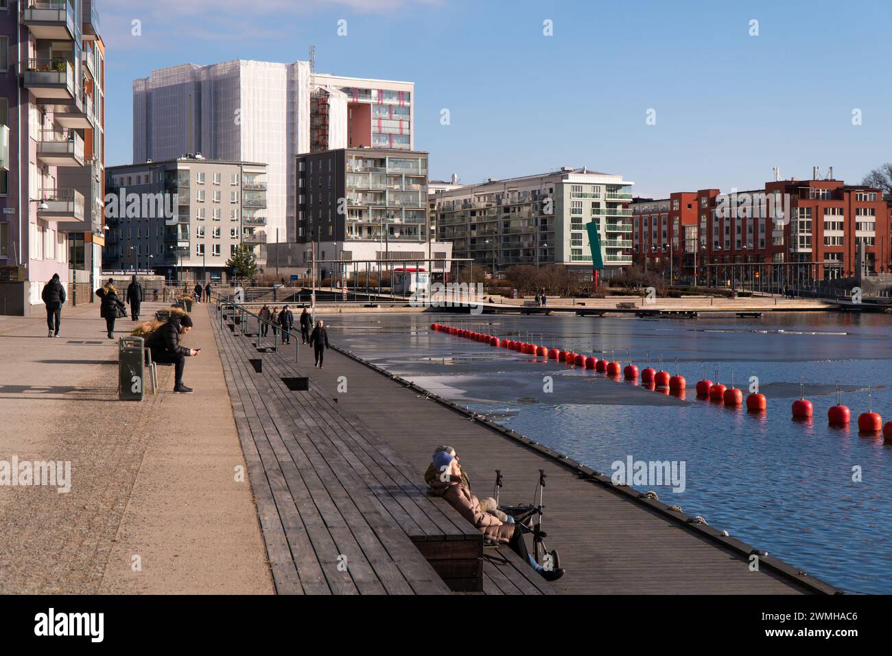 Hammarby sjöstad Bezirk, sonniger Wintertag, Menschen, die die Sonne in Stockholm genießen, in der Nähe eines Kanals und neuer moderner Gebäude. Stockfoto