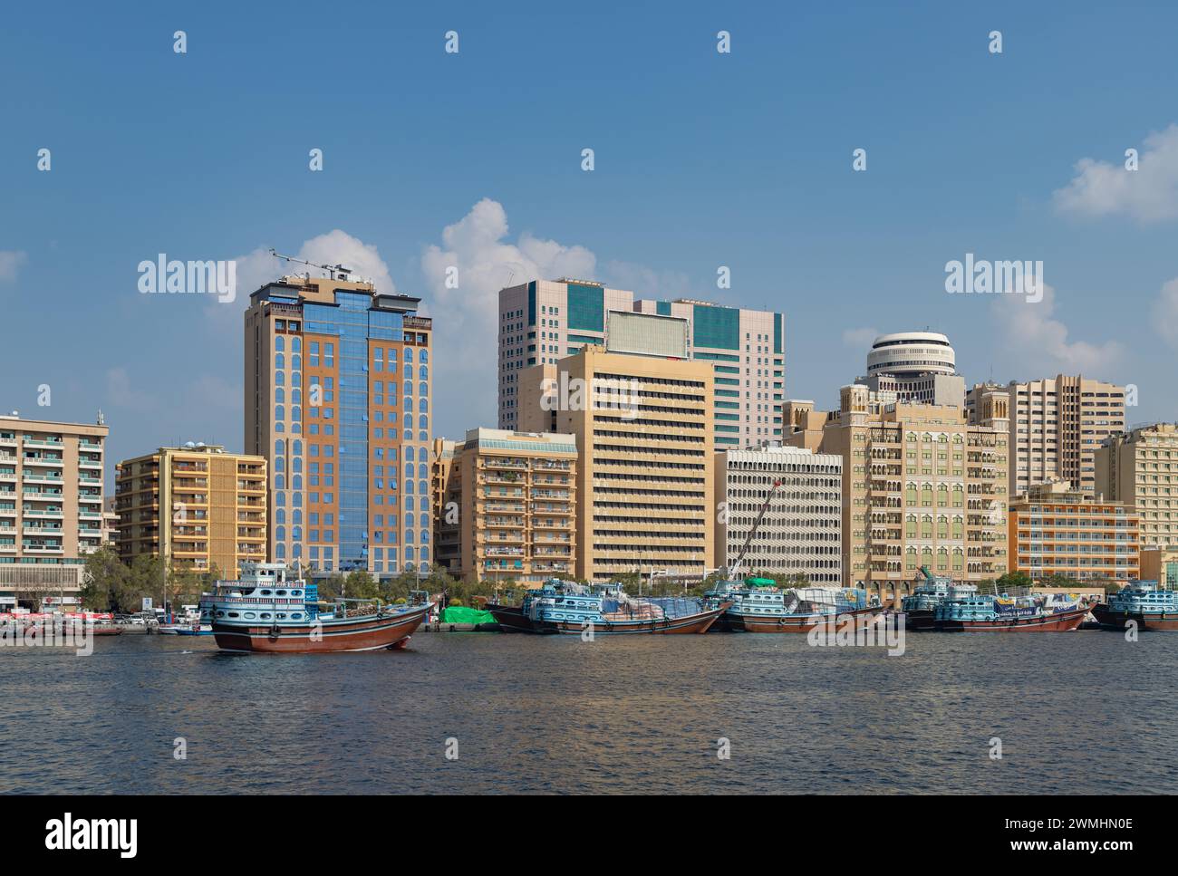 Ein Bild von einigen Gebäuden am Dubai Creek, mit einigen blauen Dhow-Booten am Rand. Stockfoto
