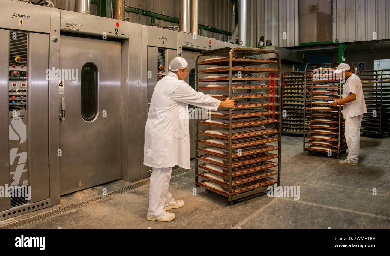 Arbeiter, die Tabletts mit Brot in einen Industrieofen legen Stockfoto