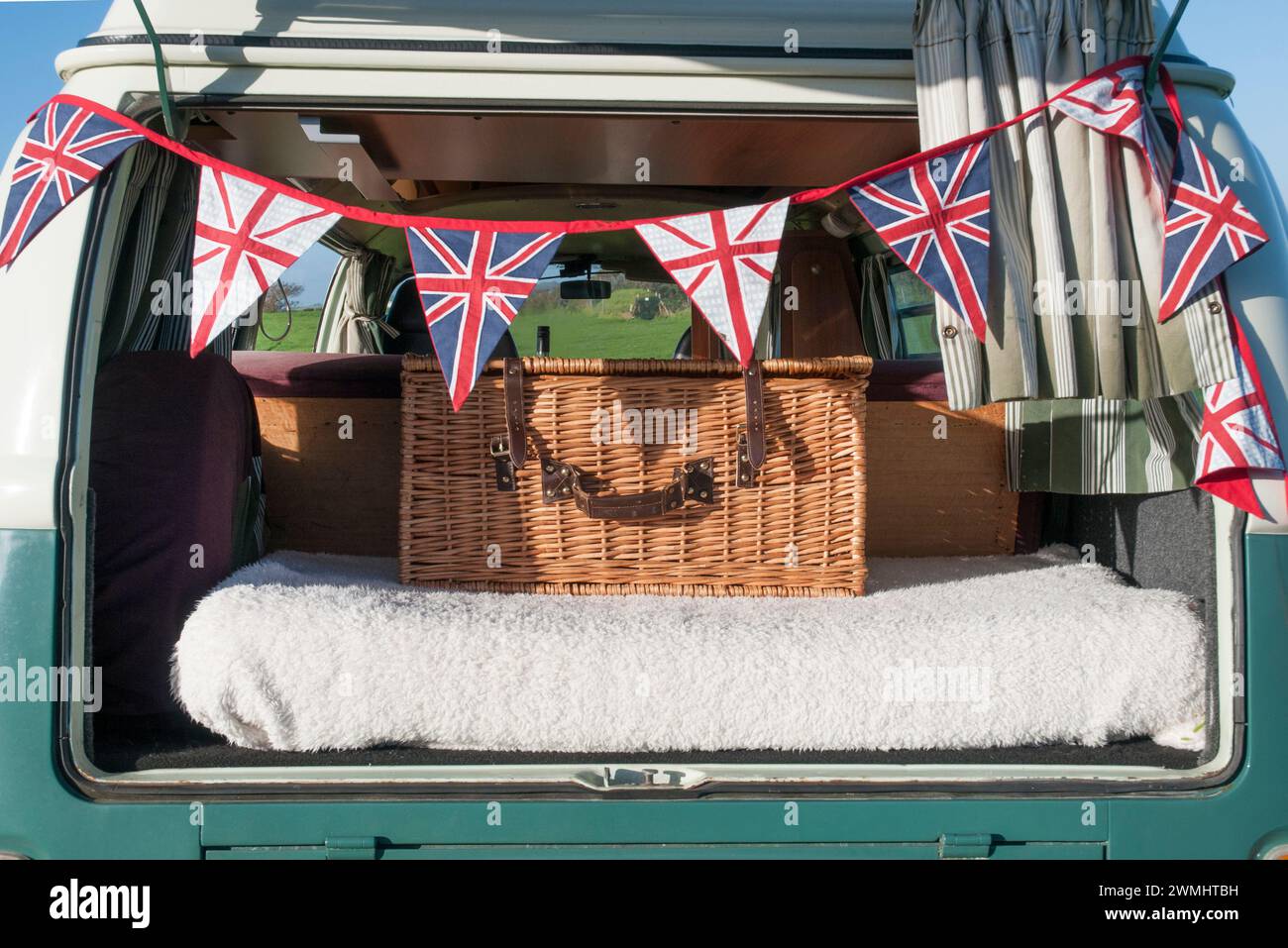 Ein Picknickkorb auf der Rückseite eines alten Wohnwagens, mit einem Flechtwerk darüber. Stockfoto