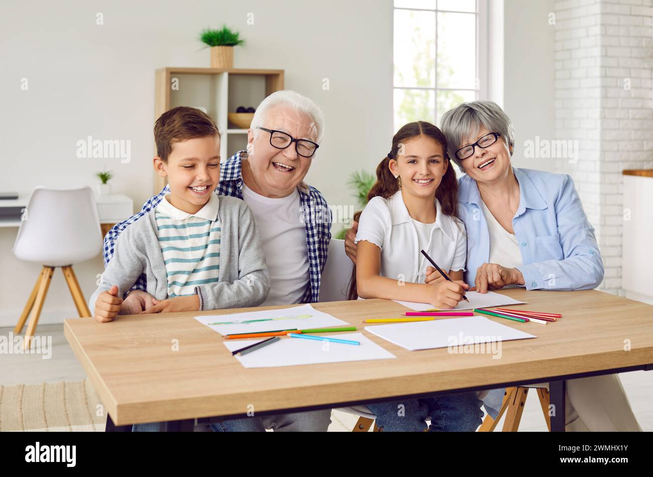 Glückliche, lächelnde Großeltern und Kinder sitzen am Tisch und zeichnen mit Bleistiften Stockfoto