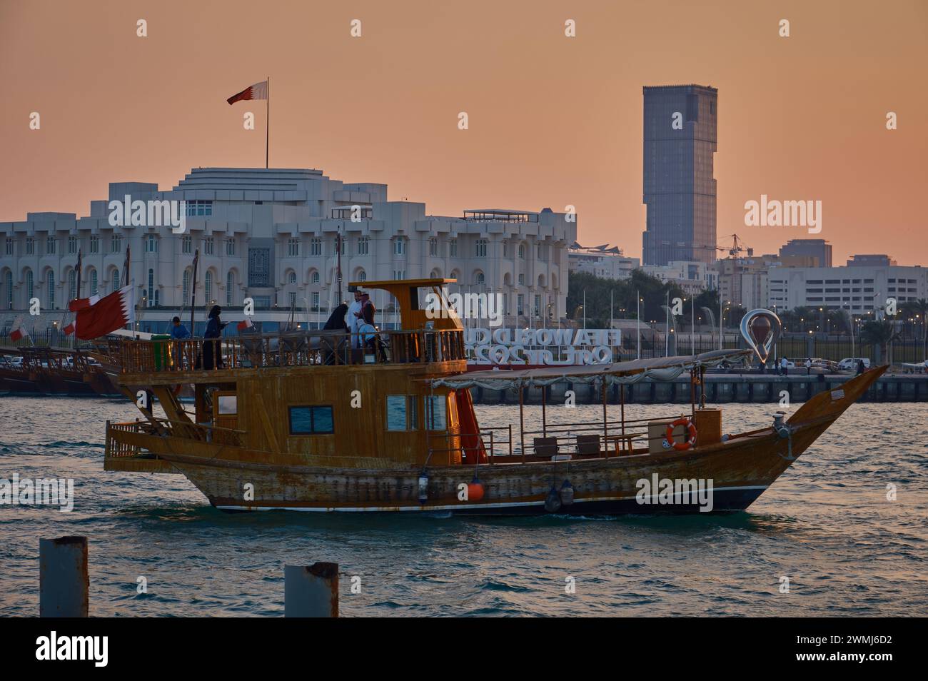Doha Corniche Sonnenuntergang mit Dhow im arabischen Golf mit der Flagge Katars, Autos auf der Straße, Menschen gehen und Amiri Diwan im Hintergrund Stockfoto