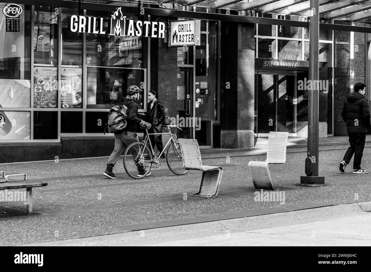 Vancouver, Kanada - 16. Februar 2024: Ein Schwarzweißbild eines Mannes, der mit seinem Fahrrad auf dem Bürgersteig der Granville Street läuft. Stockfoto