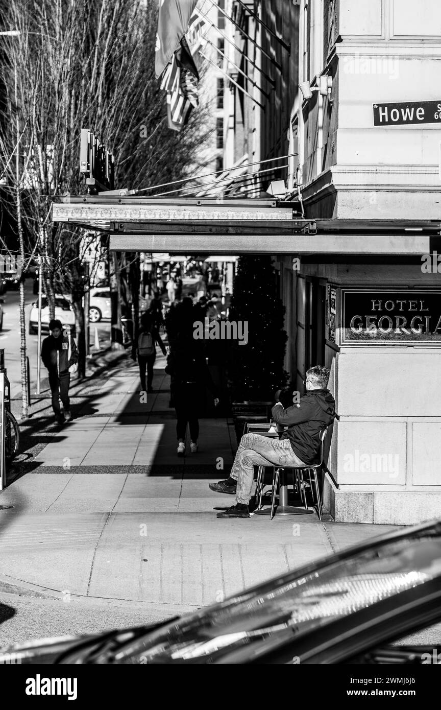 Vancouver, Kanada - 16. Februar 2024: Ein Schwarzweißbild eines Mannes, der an einem Couchtisch vor dem Hotel in Georgia sitzt und die Sonne auf den Rücken stößt Stockfoto