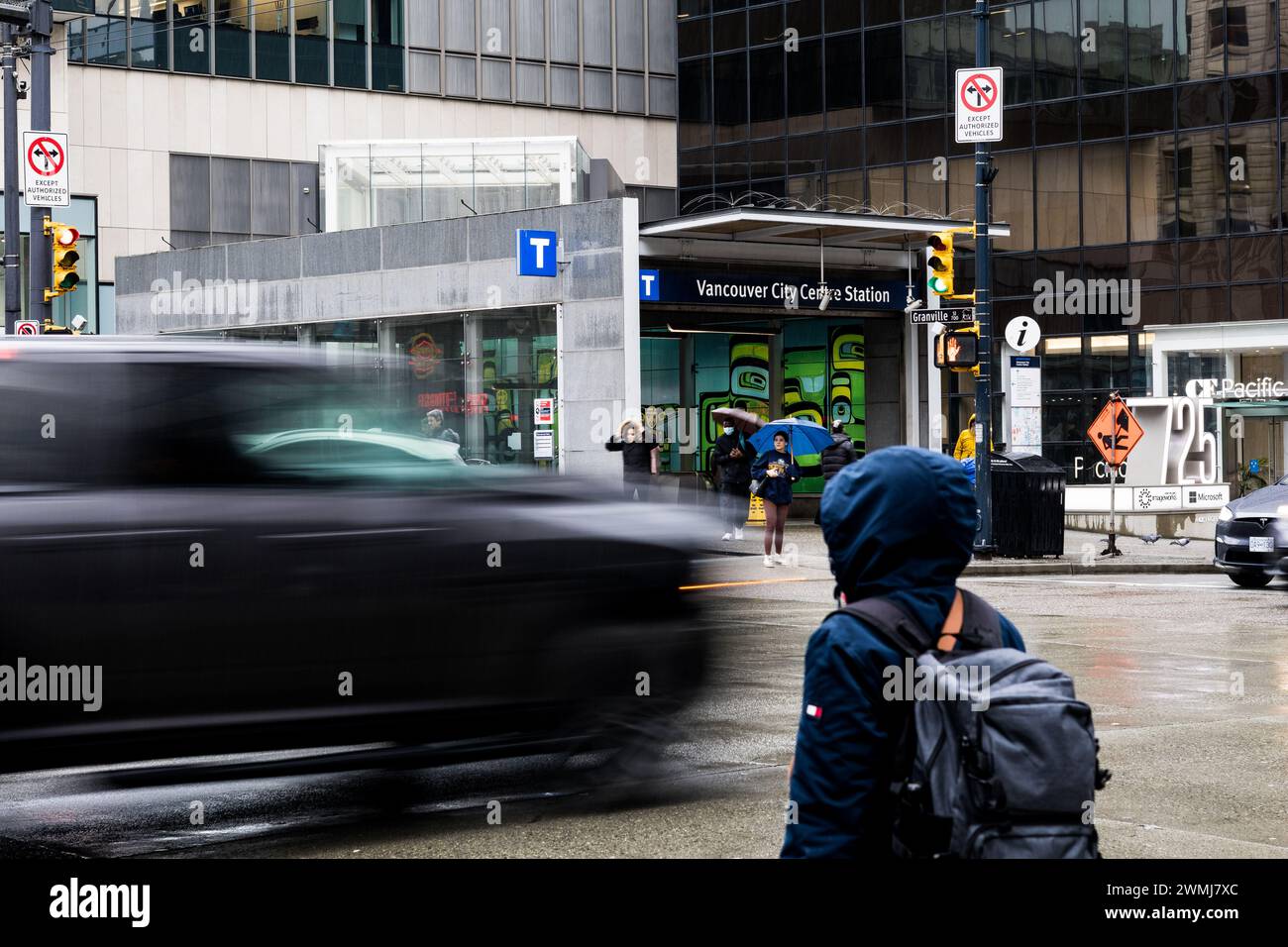 Vancouver, Kanada - 21. Februar 2024: Eine Person wartet darauf, die Georgia Street zu überqueren, mit einem vorbeifahrenden Auto, dessen Bewegung durch die langsame Verschlusszeit verschwimmt wird. Stockfoto