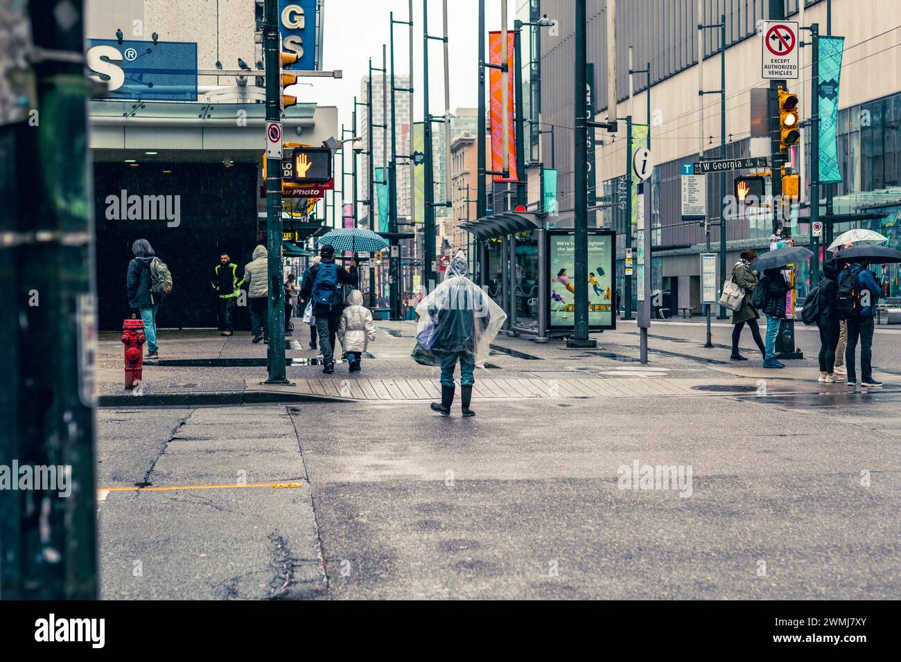 Vancouver, Kanada - 21. Februar 2024: Eine Person, die an der Verkehrsampel die Georgia Street überquert und einen transparenten Einweg-Regenponcho trägt. Stockfoto