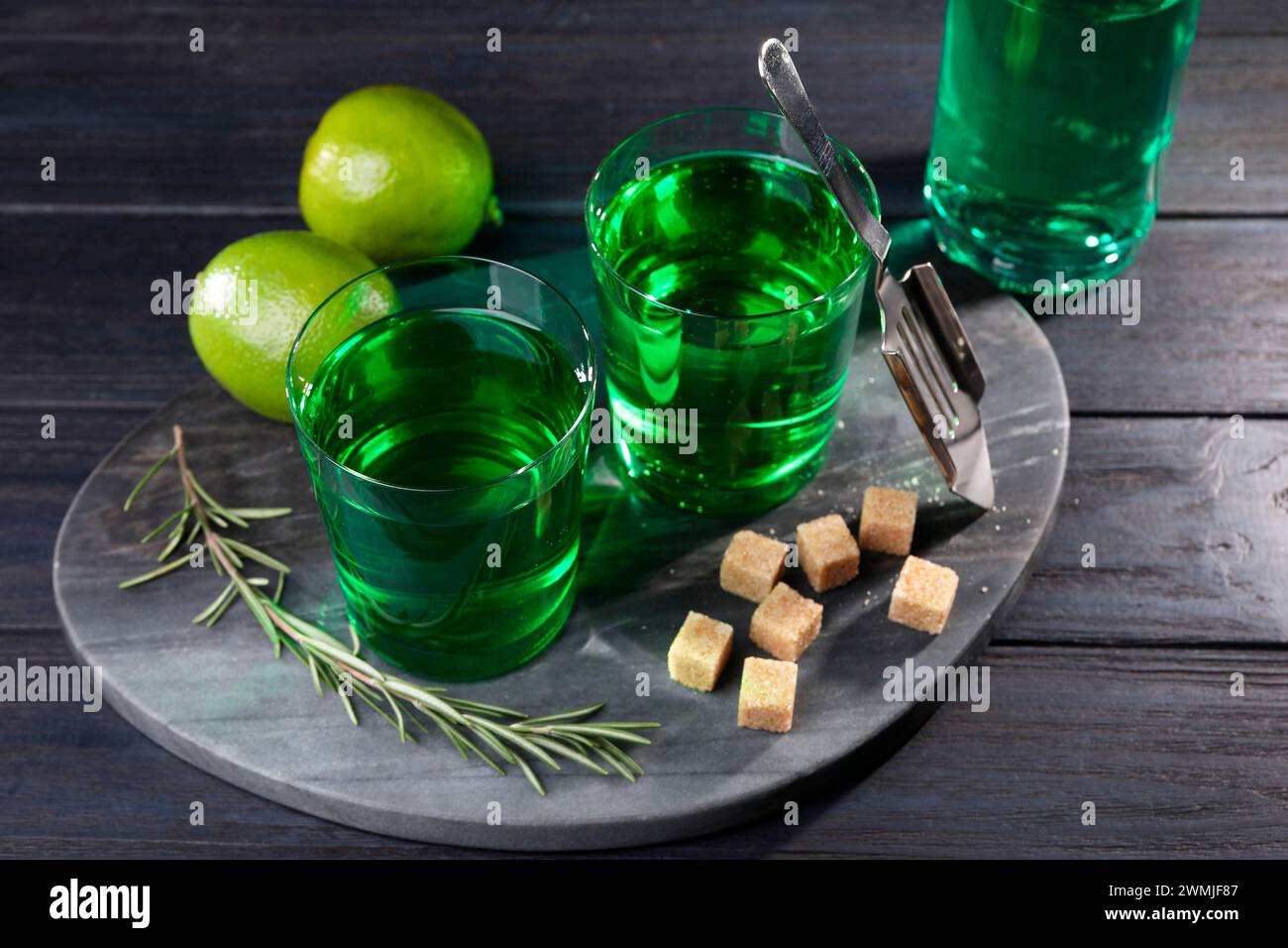 Absinth in Gläsern, Rosmarin, brauner Zucker und Limette auf Holztisch. Alkoholisches Getränk Stockfoto