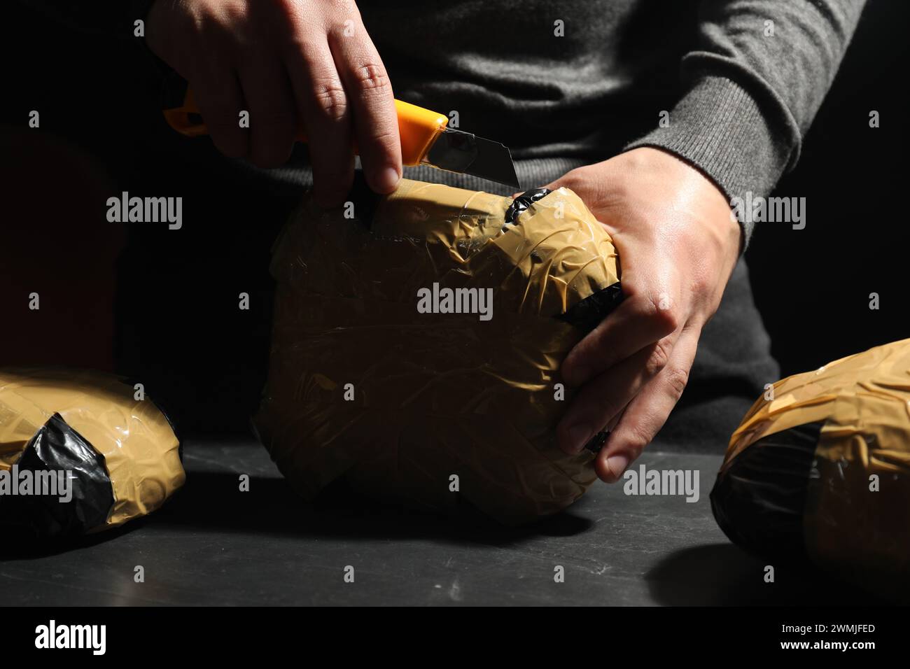 Schmuggel und Drogenhandel. Mann, der ein Paket mit Betäubungsmitteln öffnet, mit einem Koffer in der Dunkelheit, Nahaufnahme Stockfoto
