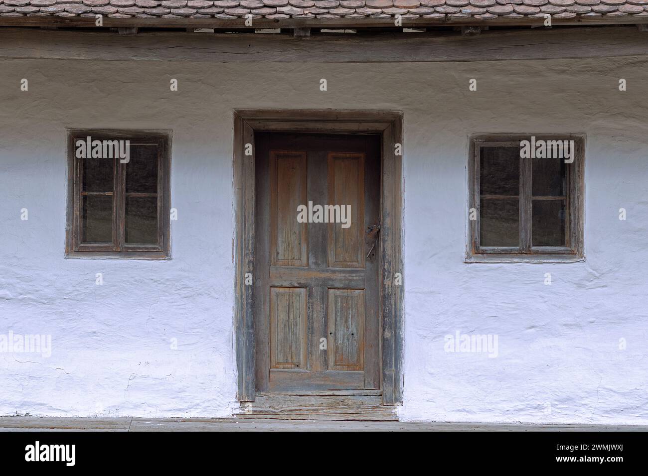 Fassade eines alten rumänischen traditionellen Hauses mit Holztür und zwei kleinen Fenstern Stockfoto
