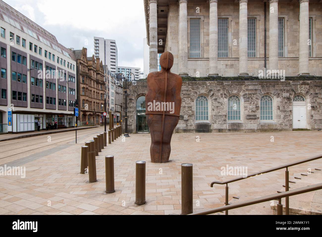 Der Eiserne Mann. Die Statue wurde 2022 wieder an einen neuen Platz gebracht und nach der Installation eines neuen Straßenbahnsystems am Victoria Square verlegt. Iron:man ist eine Statue von Antony Gormley am Victoria Square in Birmingham. Die Statue ist 6 Meter hoch, einschließlich der Füße, die unter dem Bürgersteig vergraben sind, und wiegt 6 metrische Tonnen. Die Statue neigt sich 7,5° nach hinten und 5° nach links.[1] der Bildhauer sagt, dass sie die traditionellen Fertigkeiten von Birmingham und dem Black Country repräsentieren soll, die während der industriellen Revolution praktiziert wurden. Das Rathaus von Birmingham ist zu sehen Stockfoto