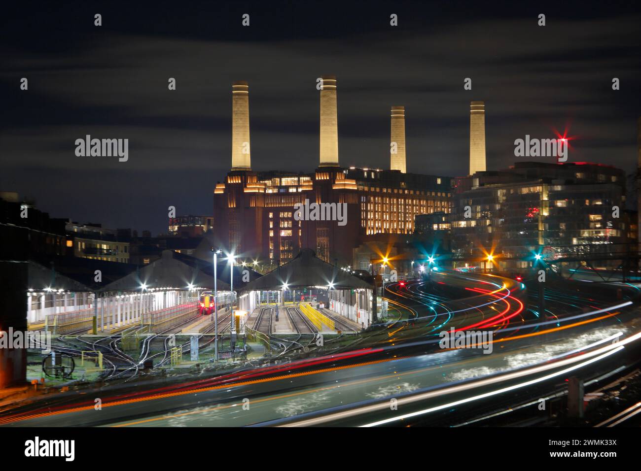 Battersea Power Station at Night, London, Großbritannien, von der Ebury Bridge Road aus, die die Eisenbahn, Motorschuppen und Lichtwege zeigt Stockfoto