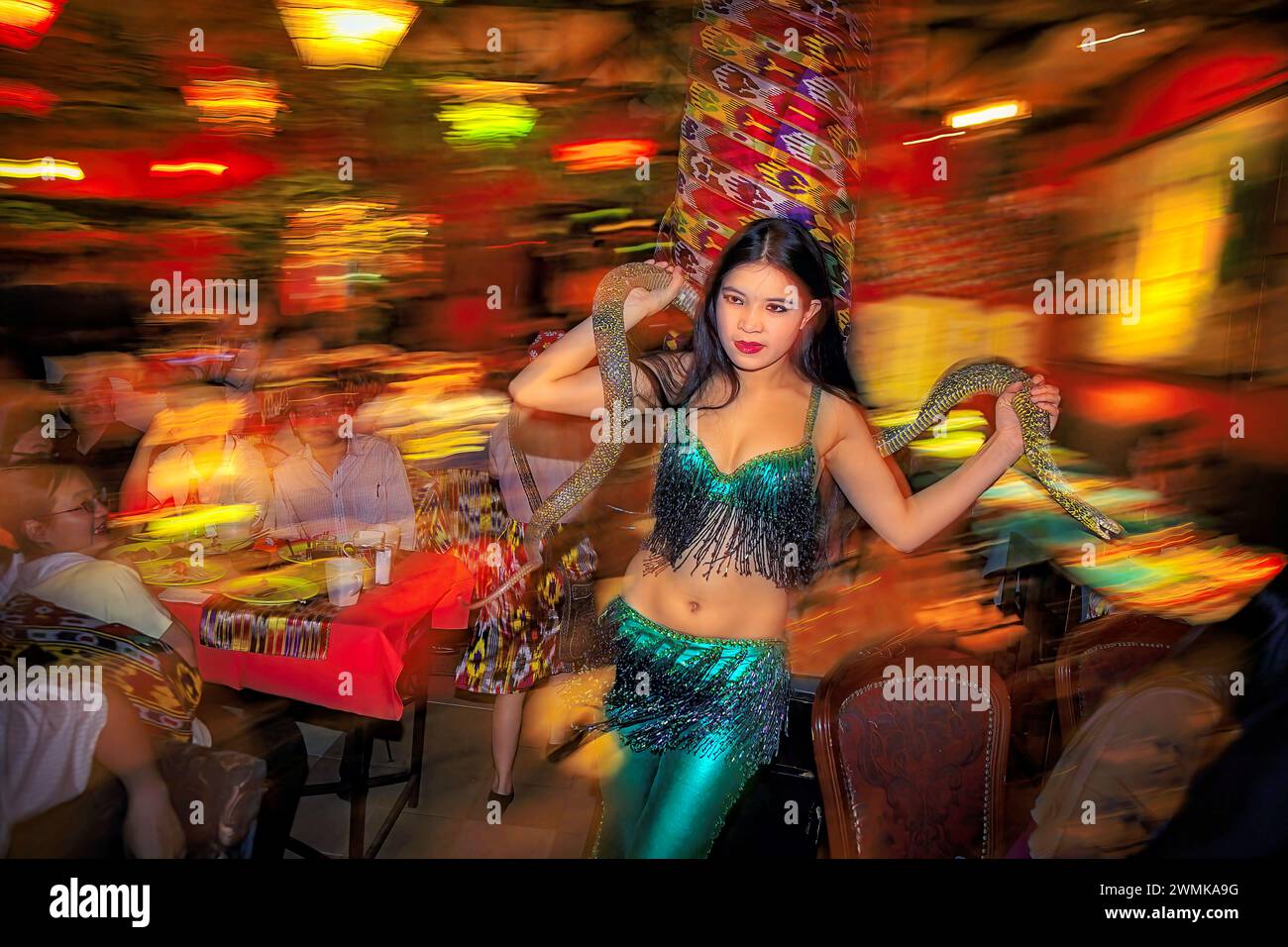 Tänzerin in grünen Glitzern und Fransen tritt mit einer Live-Schlange im Fun Ti Carnival Restaurant in Peking auf. Die Tänzer, die Kellner und die Aufführung... Stockfoto