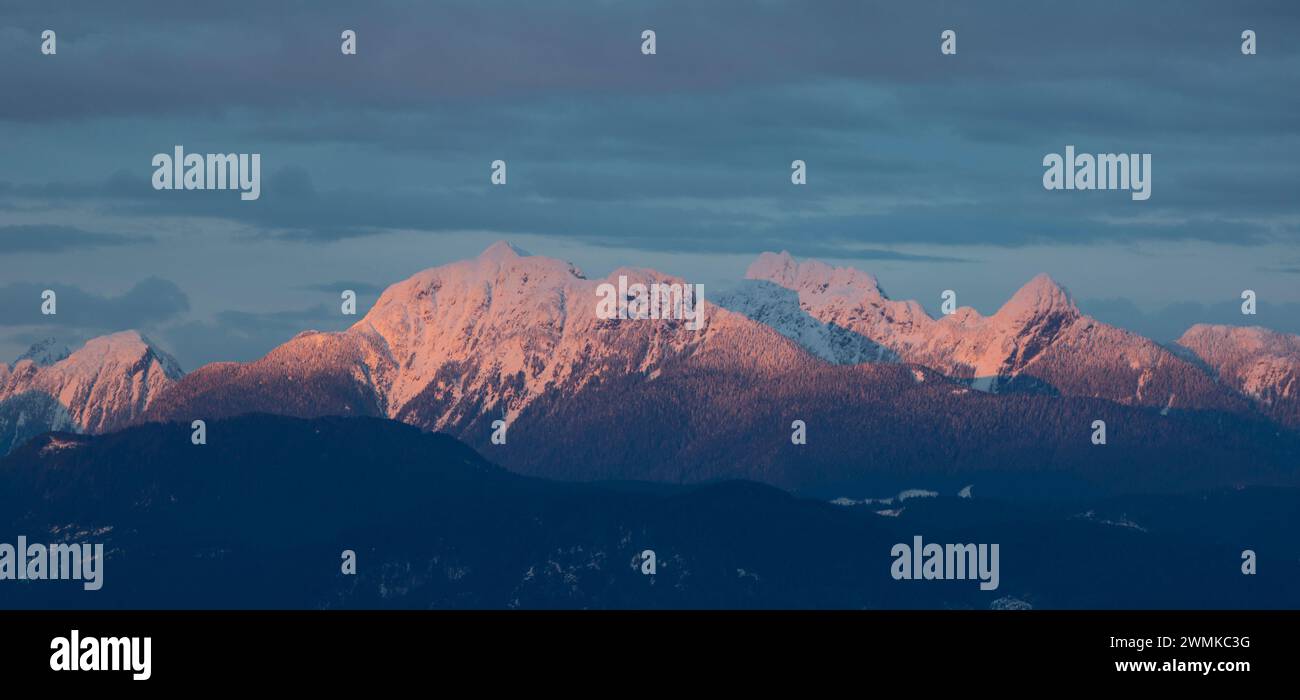 Schneebedeckte Bergkette, beleuchtet mit sanftem Licht unter blauem Himmel mit Wolken; Surrey, British Columbia, Kanada Stockfoto