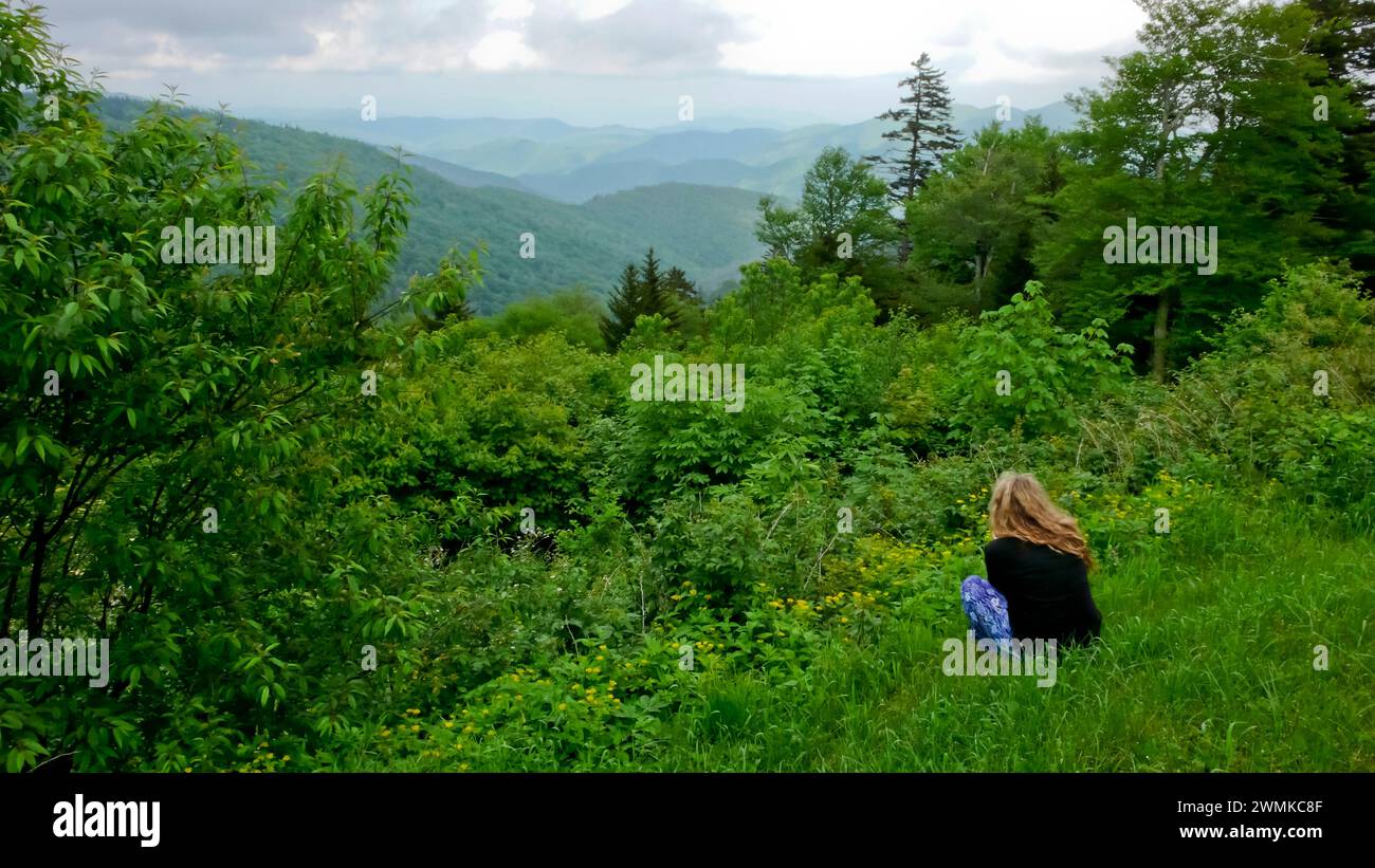 Blick von hinten auf eine Frau, die sich hinunterhockt, um den Blick auf die Blue Ridge Mountains entlang des Blue Ridge Parkway zu genießen Stockfoto
