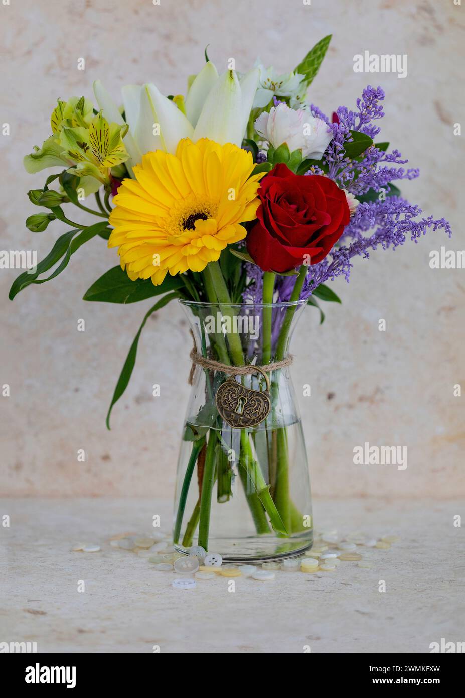 Kleiner, farbenfroher Blumenstrauß in einer Glasvase mit einem herzförmigen, dekorativen Charme, der um den Hals gebunden ist; Studio-Aufnahme Stockfoto