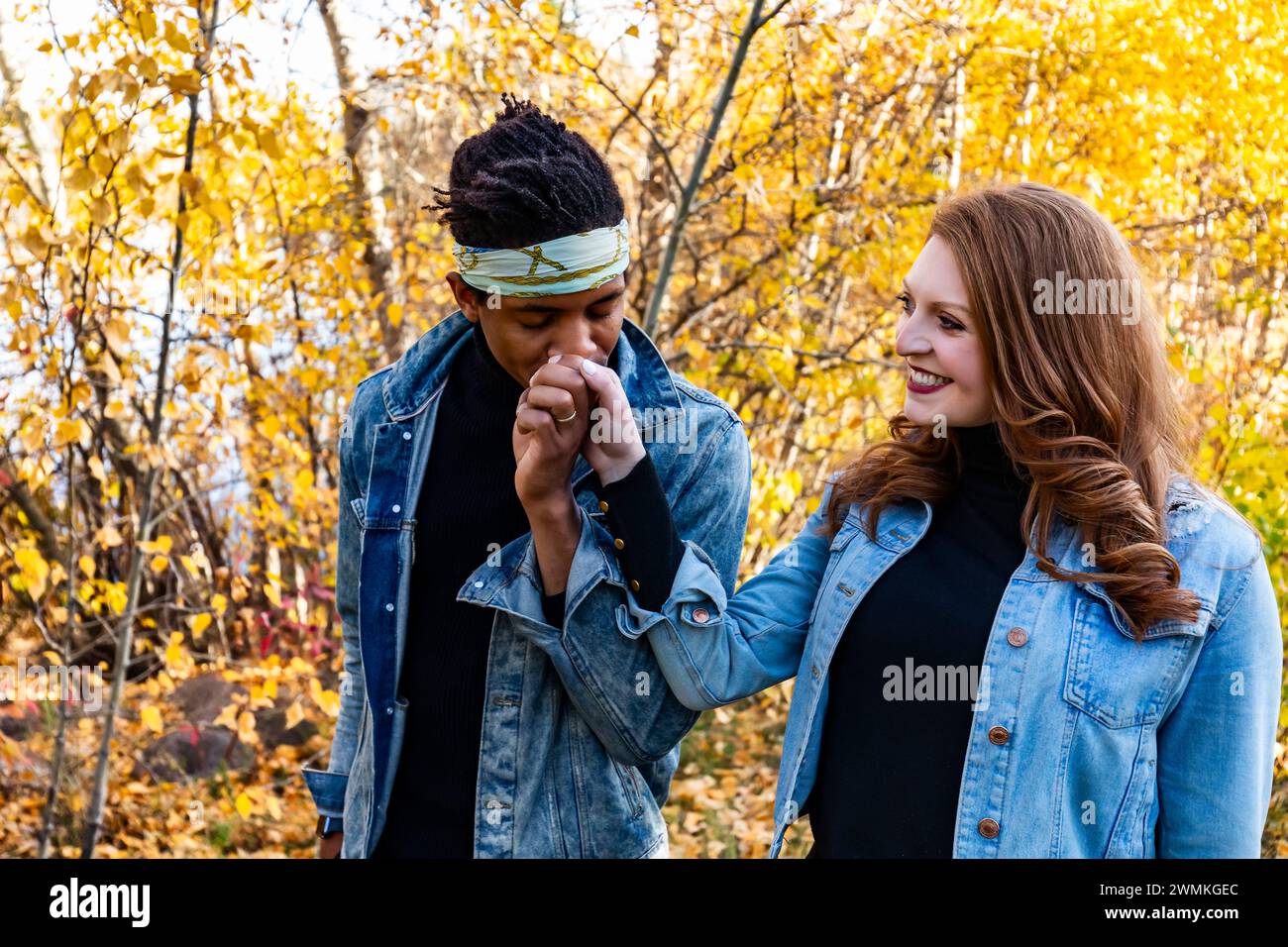 Ein Paar mit gemischter Rasse, das während eines Familienausflugs in einem Stadtpark zusammen spaziert, während der Mann seiner Frau die Hand küsst; Edmonton, Alberta, Kanada Stockfoto