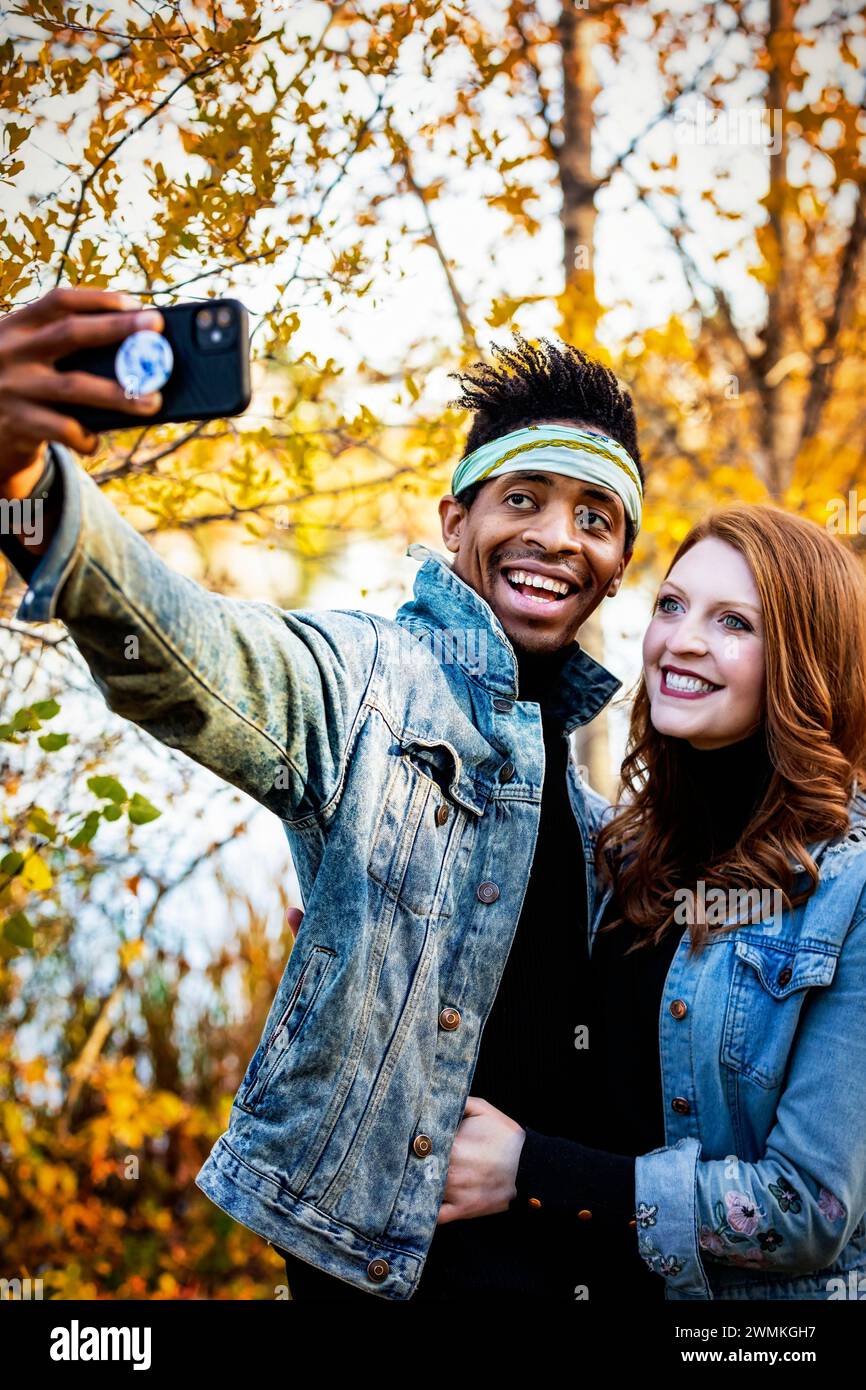 Nahaufnahme eines gemischten Rassen verheirateten Paares, das zusammen ein Selfie macht, die Handykamera anlächelt, während eines Herbstes gemeinsame Zeit verbringt... Stockfoto