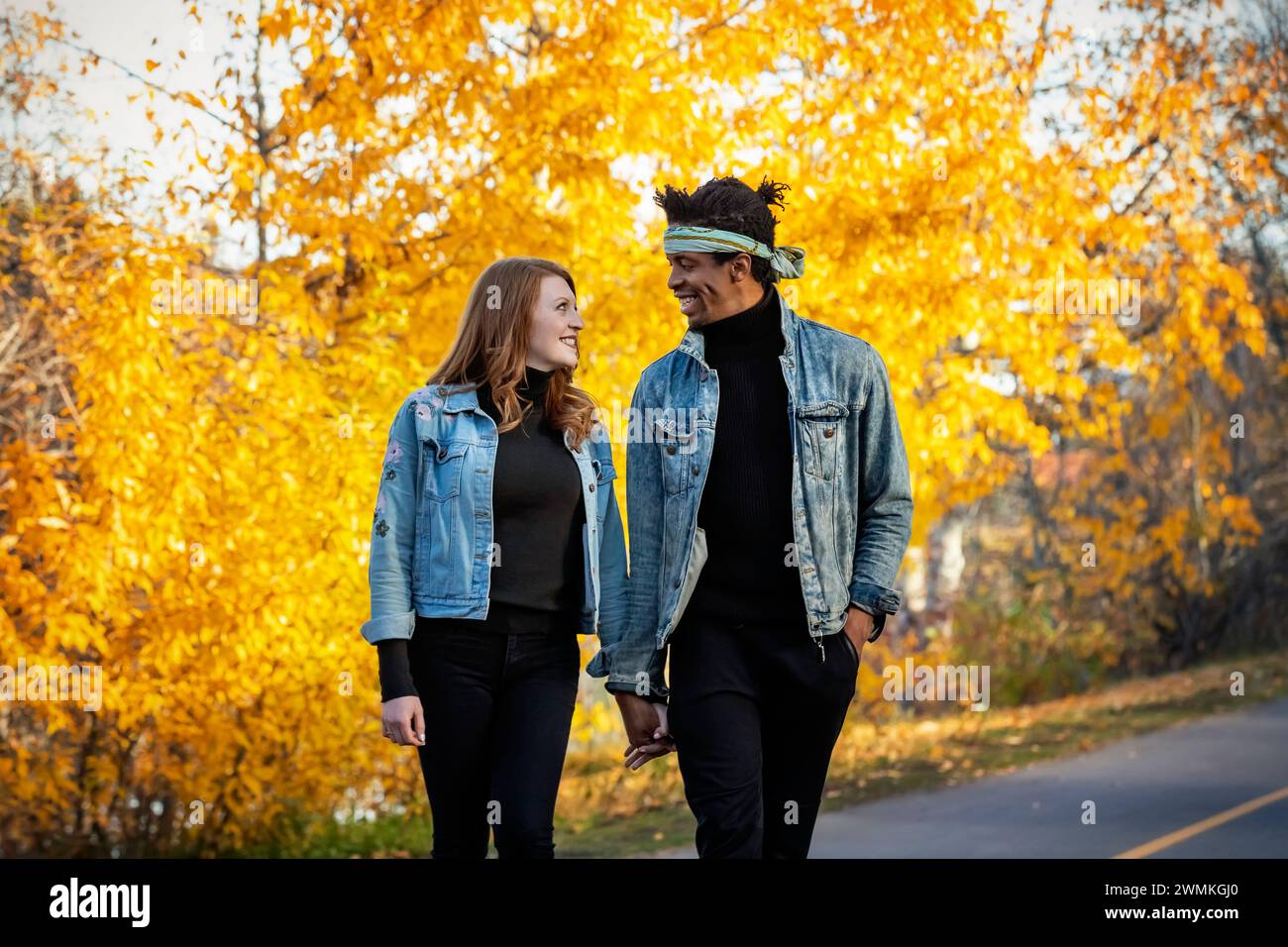 Nahaufnahme einer gemischten Rasse verheiratetes Paar, das sich anlächelt, während eines Familienausflugs im Herbst eine Straße in einem Stadtpark entlang läuft, Qualitäts-tim verbringt... Stockfoto