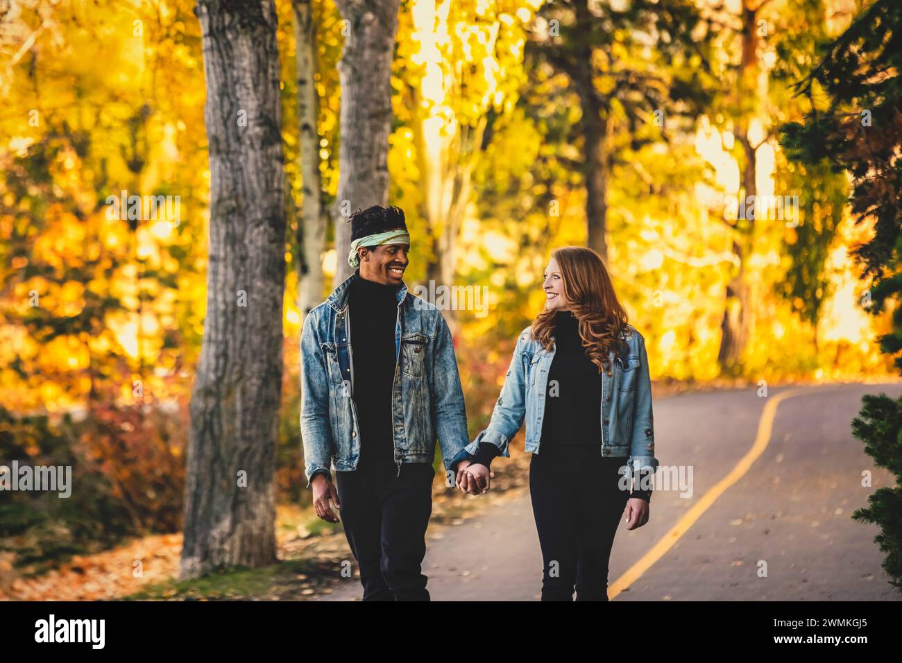 Eine gemischte Rasse heiratete ein Paar, das sich anlächelte, während eines Familienausflugs im Herbst eine Straße in einem Stadtpark entlang ging und gute Zeit miteinander verbrachte Stockfoto