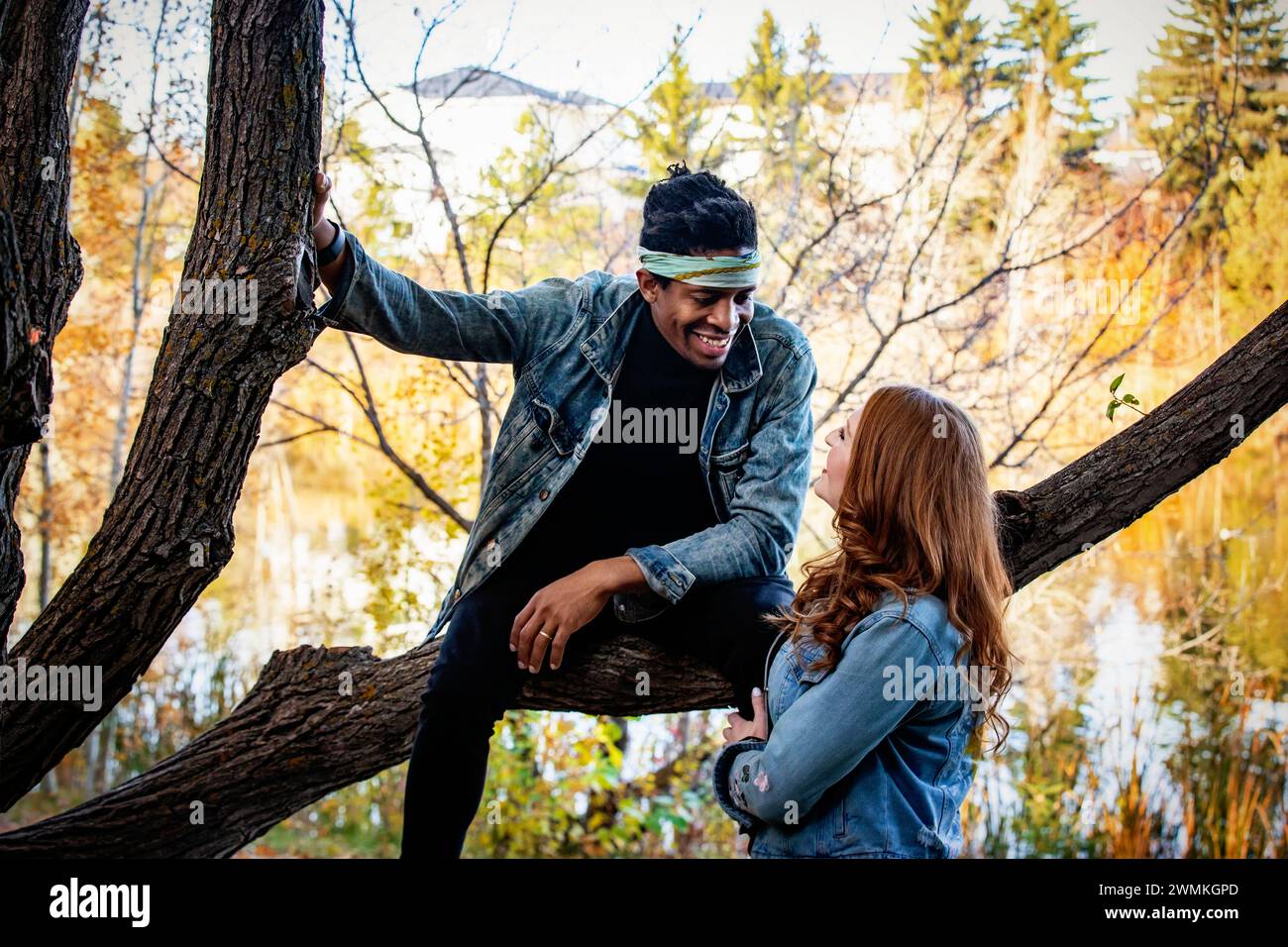 Nahaufnahme eines Paares gemischter Rassen, das sich lächelt und ansieht, während er sich auf einem Baumzweig ausruht und während eines ... zusammen gute Zeit verbringt Stockfoto