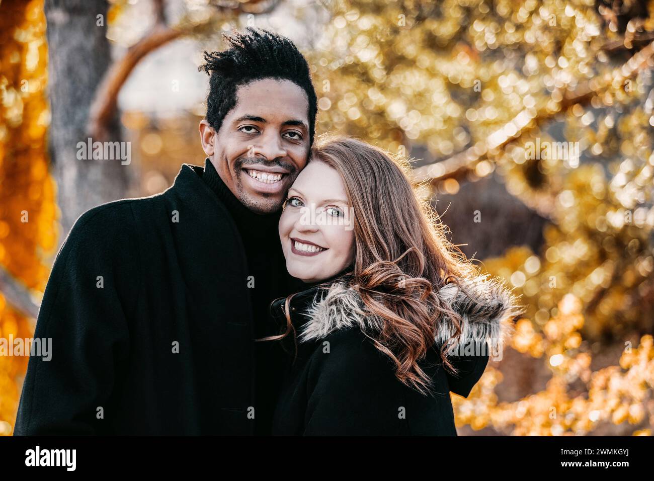 Nahaufnahme eines Paares mit gemischter Rasse, das in die Kamera lächelt und während eines Familienausflugs im Herbst in einem Stadtpark wertvolle Zeit miteinander verbringt Stockfoto