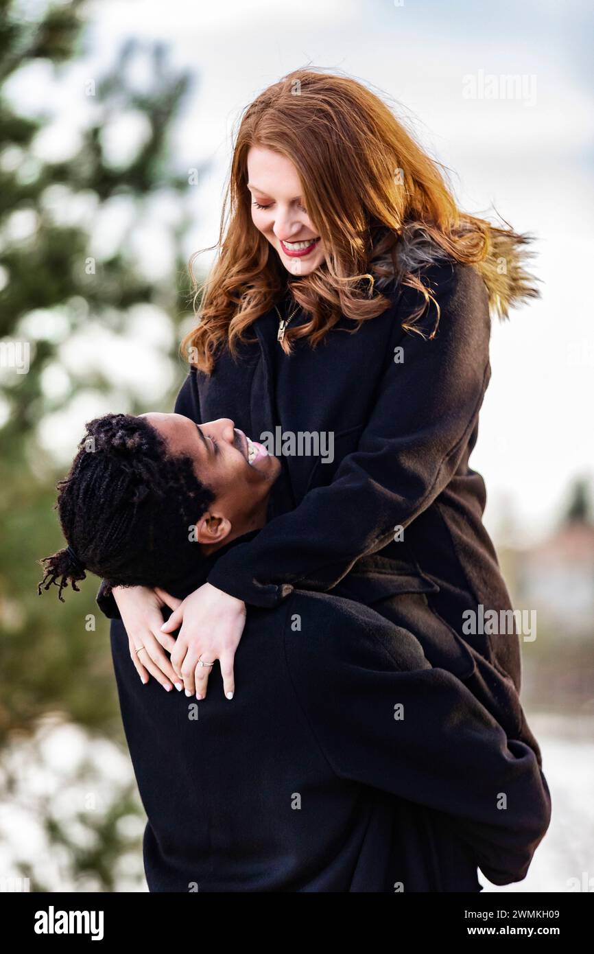 Ein Paar gemischter Rassen, Ehemann hebt seine Frau in die Arme und verbringt wertvolle Zeit zusammen während eines Familienausflugs im Herbst in einem Stadtpark Stockfoto