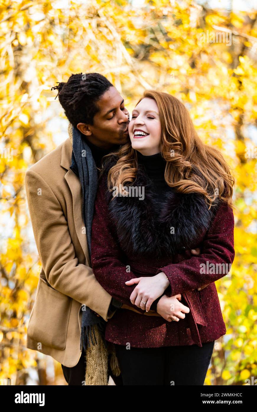 Ein gemischtes Paar, das sich umarmt und Ehemann, der seine Frau auf die Wange küsst, während er während eines Familienausflugs im Herbst in einem ci Zeit verbringt... Stockfoto