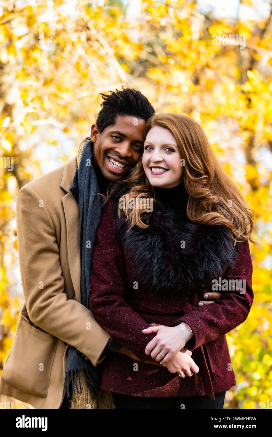 Nahaufnahme eines Ehepaares mit gemischter Rasse, das in die Kamera lächelt, während es während eines Familienausflugs im Herbst in einem Stadtpark Zeit miteinander verbringt Stockfoto