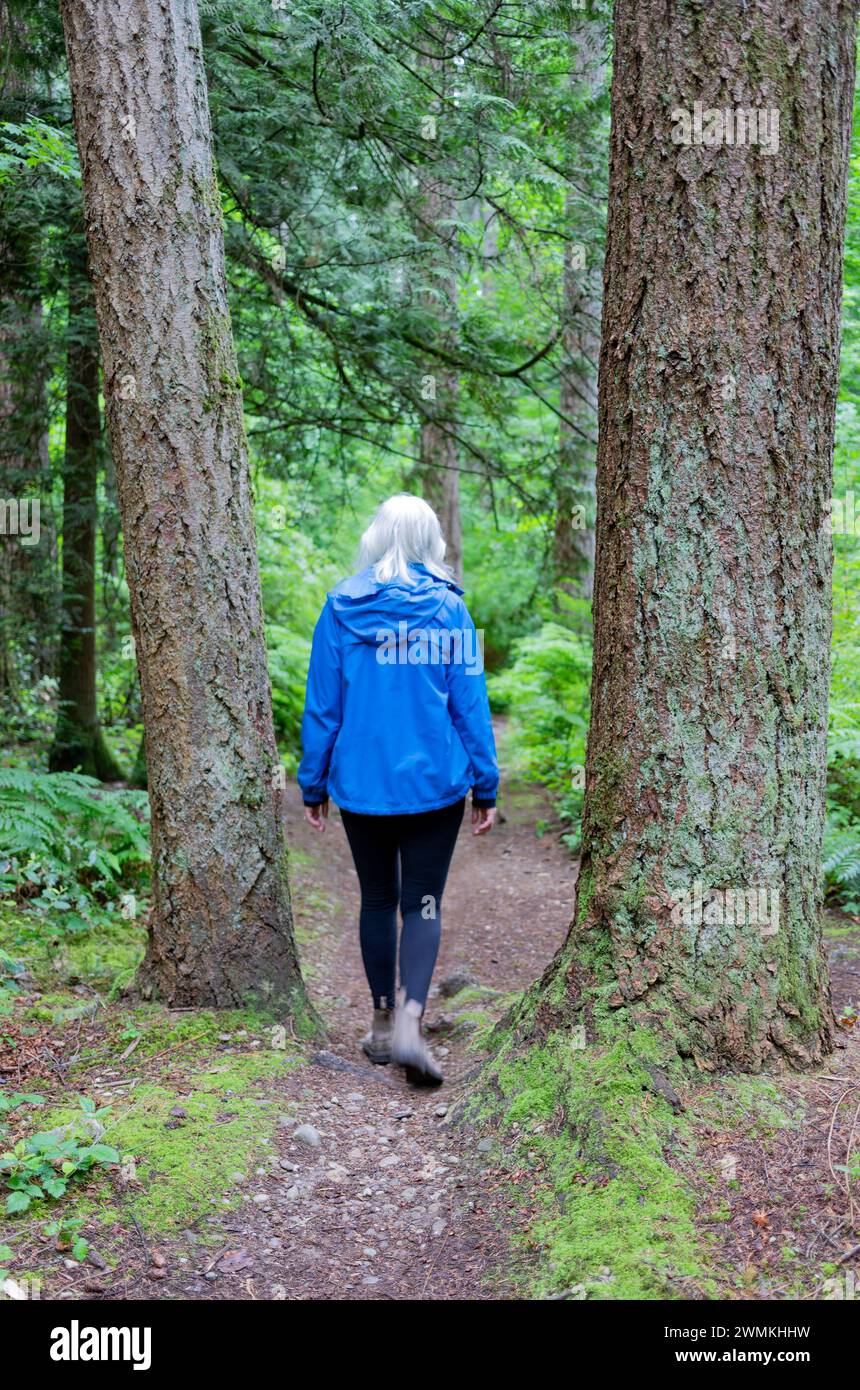 Blick von hinten auf eine Frau, die auf einem unbefestigten Pfad durch den Watershed Forest Trail geht; Delta, British Columbia, Kanada Stockfoto